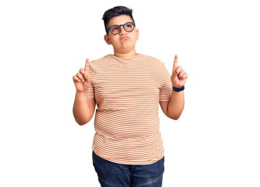 Gündelik kıyafetler giyen ve gözlük takan küçük çocuk üzgün ve üzgün görünüyor, parmaklarıyla yön gösteriyor, mutsuz ve depresif.. 