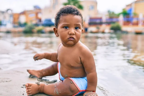 愛らしいアフリカ系アメリカ人の幼児がビーチに座っています — ストック写真
