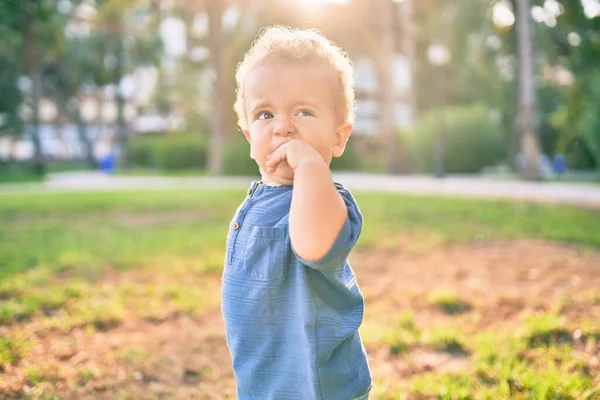 在阳光灿烂的日子里 公园里的牙疼 让可怜的小男孩用手指捂住嘴 摸着牙龈 漂亮的金发碧眼的男婴在户外痛苦地寻找新的婴儿牙 — 图库照片