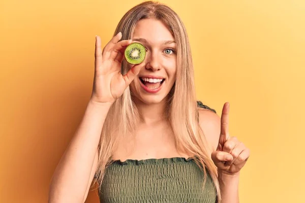 Young Blonde Woman Holding Kiwi Smiling Idea Question Pointing Finger — ストック写真