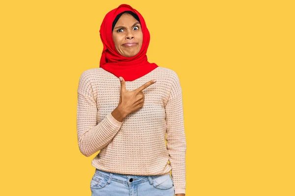 身穿传统伊斯兰头巾的年轻非洲裔美国妇女带着食指 忧心和惊讶的表情 将焦虑和紧张抛在一边 — 图库照片