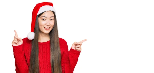 若い中国の女性は さまざまな方向に指で自信を持って指して笑顔クリスマスの帽子を着用 広告のコピースペース — ストック写真