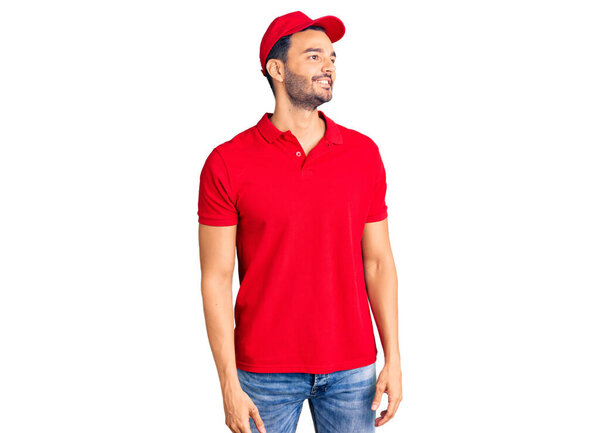 Young handsome hispanic man wearing delivery courier uniform looking away to side with smile on face, natural expression. laughing confident. 