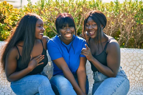 公園のベンチに座って幸せそうに笑っている3人のアフリカ系アメリカ人の友人 — ストック写真