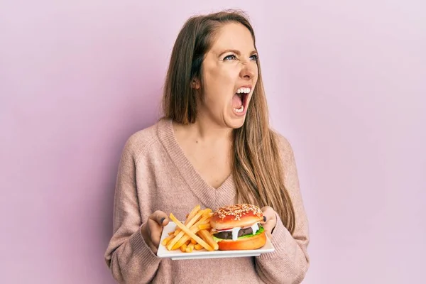 Young Blonde Woman Eating Tasty Classic Burger Fries Angry Mad — Stock Photo, Image