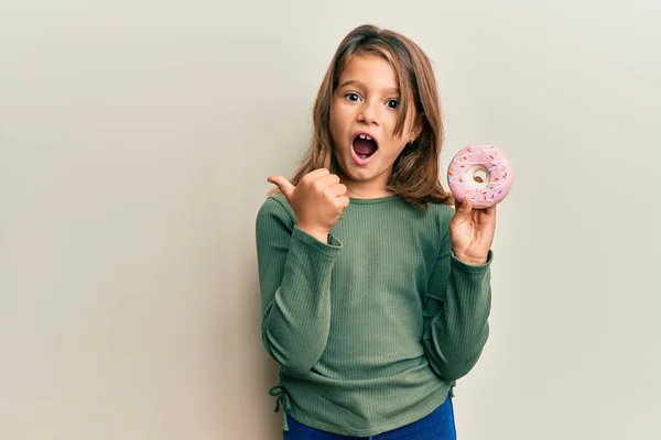 Little Beautiful Girl Gospodarstwa Smaczne Kolorowe Pączki Wskazując Kciuk Góry — Zdjęcie stockowe