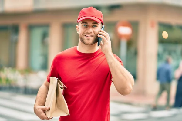 Junger Kaukasischer Auslieferer Spricht Auf Dem Smartphone Und Hält Papiertüte — Stockfoto