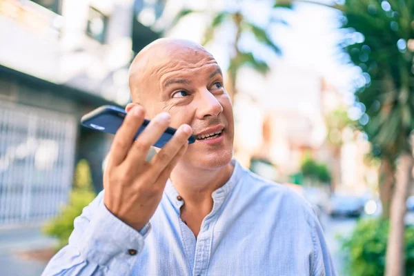 Middle age bald man smiling happy sending audio message using smartphone at the city.