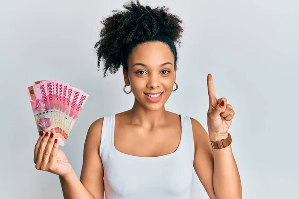 Chica Afroamericana Joven Sosteniendo Billetes Rupias Indonesias Sonriendo Con Una —  Fotos de Stock