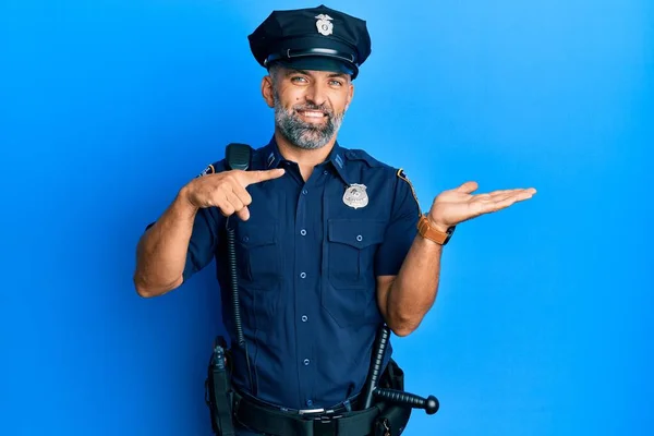 Middle age handsome man wearing police uniform amazed and smiling to the camera while presenting with hand and pointing with finger.