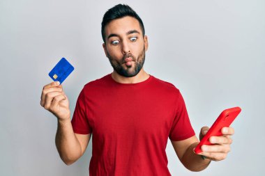 Genç İspanyol adam elinde akıllı telefon ve kredi kartı ile balık suratlı ve şaşı gözlü, çılgın ve komik.. 
