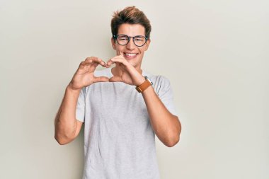 Sıradan kıyafetler ve gözlüklerle gülümseyen yakışıklı beyaz adam elleriyle kalp sembolü yapıyor. romantik kavram. 