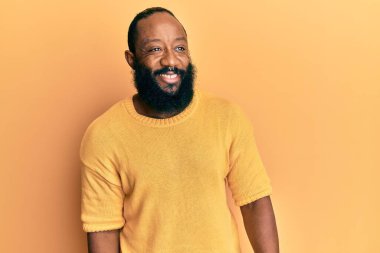 Genç Afro-Amerikan bir adam günlük kıyafetler giyip yüzünde gülümseme, doğal bir ifade ile yan yana bakıyor. Kendinden emin gülen. 