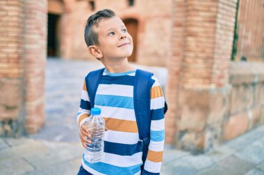 Sevimli beyaz çocuk gülümsüyor. Şehirde elinde bir şişe su tutuyor..
