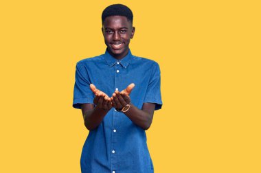 Elleri avuçlarında gülümseyen ve el hareketi yapan gündelik giysiler giyen genç Afro-Amerikan bir adam. Bekleme ve koruma 