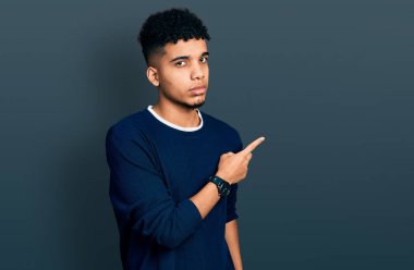 Genç Afro-Amerikalı, günlük kıyafetler giymiş, elini kaldırmış, ciddi ve sakin bir yüz ifadesi sergiliyor. 