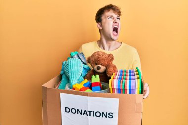 Kafkasyalı genç adam elinde oyuncaklarla dolu bir bağış kutusu tutuyor kızgın ve öfkeli çığlıklar atıyor öfkeyle bağırıyor, öfkeyle yukarı bakıyor.. 