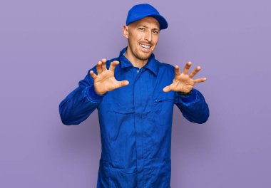 Sakallı kel adam, inşaatçı tulumu giyiyor komik bir şekilde gülümsüyor kedi gibi pençe hareketi yapıyor, agresif ve seksi bir ifade. 