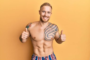 Mayosuz mayo giyen beyaz bir genç, elinde olumlu bir jest yapıyor, gülümsüyor ve mutlu. Neşeli ifade ve kazanan jest. 