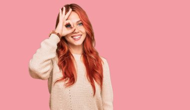 Genç kızıl saçlı kadın, sıradan bir kazak giyiyor. El hareketleriyle gülümsüyor. Gözleri, mutlu yüzüyle parmaklarının arasından bakıyor.. 