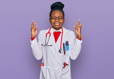 Genç Afro-Amerikan kadın doktor üniforması giyiyor ve steteskop işareti yapıyor umut ve gözler kapalı gülümseyerek. Şans ve batıl inançlar. 