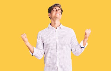 İş kıyafetleri ve gözlük takan yakışıklı genç adam çok mutlu ve heyecanlı. Kolları havada, gülümseyen ve başarı için çığlık atan kazanan bir jest yapıyor. kutlama konsepti. 