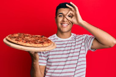 İtalyan pizzası tutan genç Arap adam gülümsüyor. Mutluluktan gülümsüyor. 