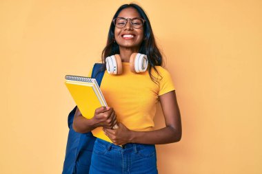 Öğrenci çantası ve kitapları tutan genç Hintli kız. Olumlu ve mutlu görünüyor. Kendine güvenen bir gülümsemeyle dişlerini gösteriyor. 