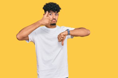 Genç Arap adam, günlük beyaz tişört giyip baş parmak kaldırıyor, anlaşmazlık ve anlaşma ifadesi takınıyor. çılgın çatışma 