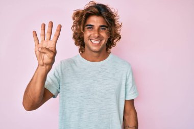 İspanyol asıllı genç adam, gündelik giysiler giyip dört numarayı gösterip işaret ederken kendinden emin ve mutlu bir şekilde gülümsüyor.. 