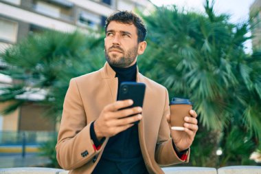 Zarif ceketli yakışıklı bir iş adamı. Açık havada akıllı telefon kullanıyor.