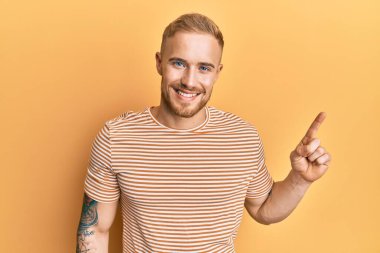 Sıradan çizgili tişört giyen genç beyaz bir adam bir fikir ya da soruyla gülümsüyor ve mutlu bir yüzle işaret ediyor. 