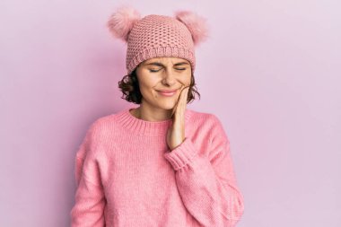 Genç esmer kadın, diş ağrısı ya da diş hastalığından dolayı şirin yün şapkalar takıp ağızlarına acı dolu bir ifadeyle dokunuyor. dişçi 