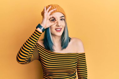 Genç modern kız yün şapka takıyor. El hareketleriyle gülümsüyor, gözleriyle mutlu yüzlere bakıyor.. 