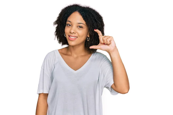 カジュアルな服を着た若いアフリカ系アメリカ人の少女が笑顔で 指を見てカメラで小さなサイズのサインをして手で自信を持ってジェスチャーをしています 概念を測定し — ストック写真