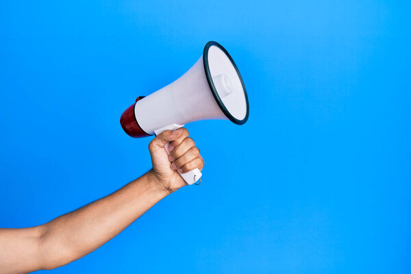 Латиноамериканец держит мегафон на изолированном синем фоне.