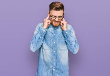 Genç, kızıl saçlı bir adam, yüksek sesli müzik sesi için kulaklarını parmaklarıyla kapatıyor. sağır kavramı. 