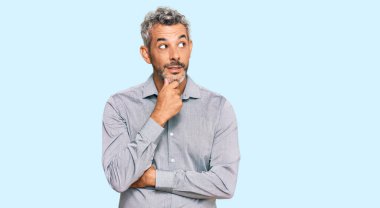 Orta yaşlı, gri saçlı, sıradan kıyafetler giyen, elleri çenesinde soru soran, düşünceli bir adam. Düşünceli bir yüzle gülümsüyor. şüphe kavramı. 