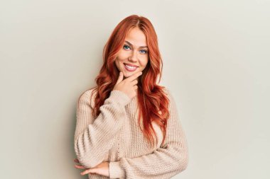 Genç, güzel, kızıl saçlı, sıradan bir süveter giyen, kameraya kendinden emin, kollarını kavuşturmuş ve çenesini kaldırmış gülümseyen bir kadın. Olumlu düşünmek. 