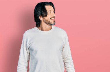 Orta yaşlı, günlük kıyafetler giyen, yüzünde gülümseme ve doğal ifadeyle yan yana bakan beyaz bir adam. Kendinden emin gülen. 