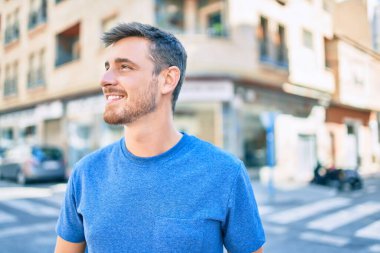 Genç beyaz adam gülümseyerek şehirde mutlu mesut yürüyor..