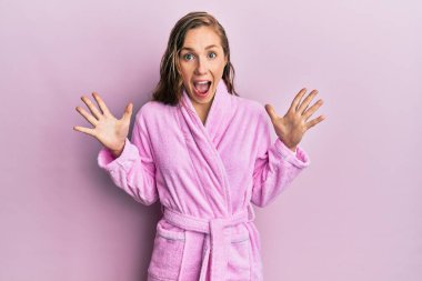 Bornoz giyen genç sarışın kadın çılgınlığı kutluyor ve başarıya hayret ediyor kollarını kaldırıyor ve gözleri açık heyecanla haykırıyor. Kazanan konsept 