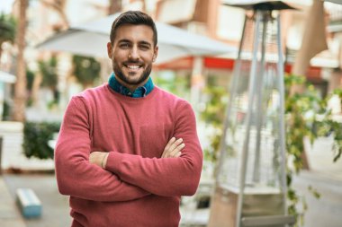 Kollarını kavuşturup gülümseyen genç İspanyol adam şehirde mutlu bir şekilde duruyor..