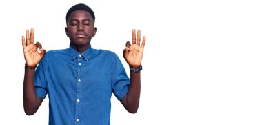 Rahat kıyafetler giyen, gözleri kapalı gülümseyen genç Afro-Amerikalı adam parmaklarıyla meditasyon hareketi yapıyor. yoga konsepti. 