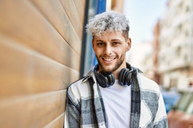 Şehirde kulaklık takarak mutlu gülümseyen genç İspanyol adam..