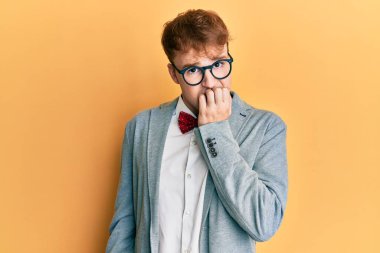 Genç, beyaz, inek, gözlüklü, hippi görünümlü, papyonlu, gergin ve ağzı tırnak yiyen bir adam. anksiyete. 