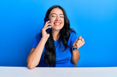 Güzel esmer genç bir kadın akıllı telefonda konuşuyor gururla bağırıyor, zaferi kutluyor ve başarıyı kollarını kaldırarak kutluyor. 