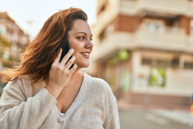 Genç İrlandalı artı cüsseli kız gülümseyerek şehirde akıllı telefondan konuşmaktan mutlu oluyor..