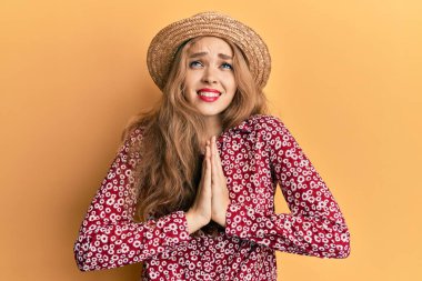 Güzel sarışın, beyaz kadın yaz şapkası takıyor. Elleriyle yalvarıyor ve dua ediyor. Yüzünde umut ifadesi var. Yalvarıyor. 