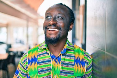 Genç Afrikalı Amerikalı gülümseyen mutlu bir adam şehrin duvarına yaslanıyor..